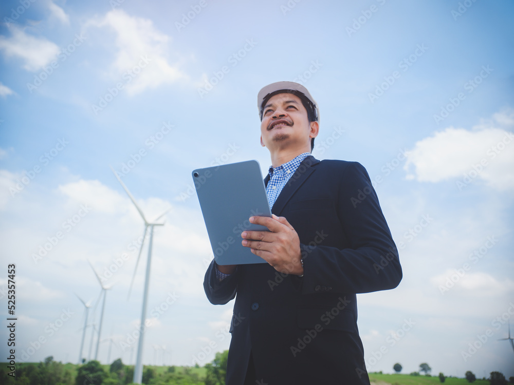 Successful engineer manager stand holding tablet front the wind turbines generating electricity power station. Concept of sustainability development by alternative energy
