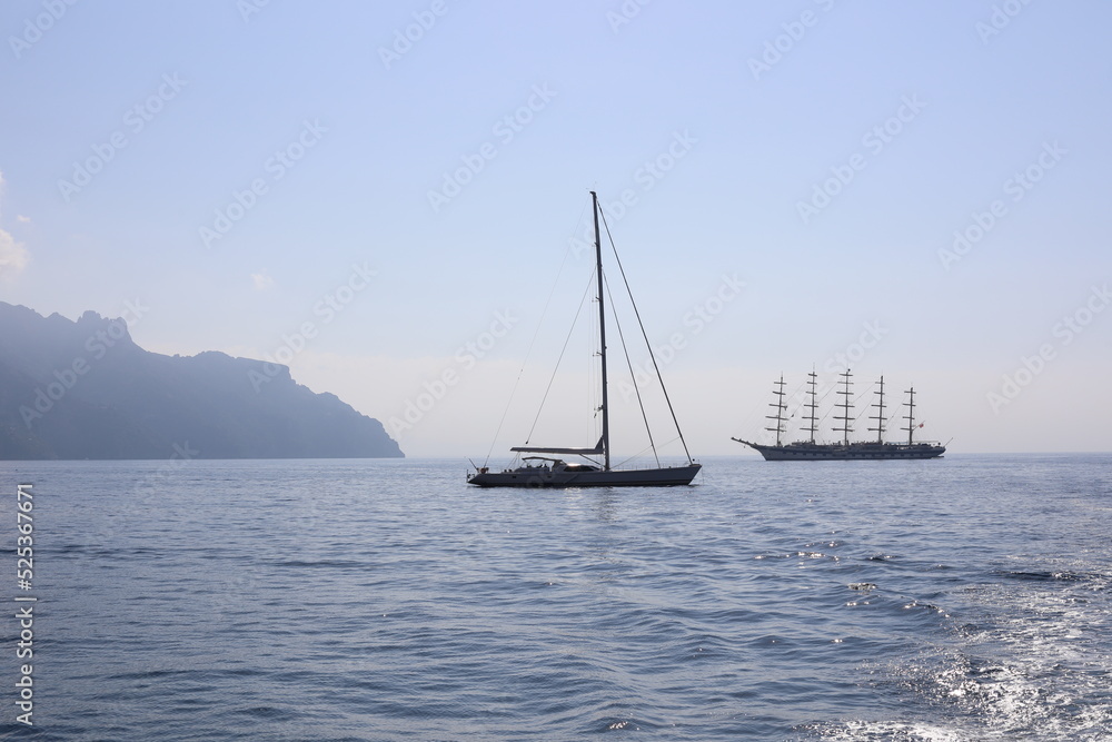 Beautiful seascape with yacht near shore in the sea. Modern sailboat on a sunny summer day.  Sailing near coastline in the Mediterranean Sea. Scenic Amalfi Coast view.