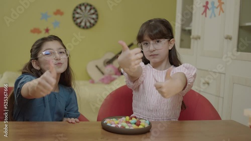 Little girls take a break from school homework classes and eat colorful candies. Little girlfriends eating colorful candies on the table in her room, laughing and having fun together.