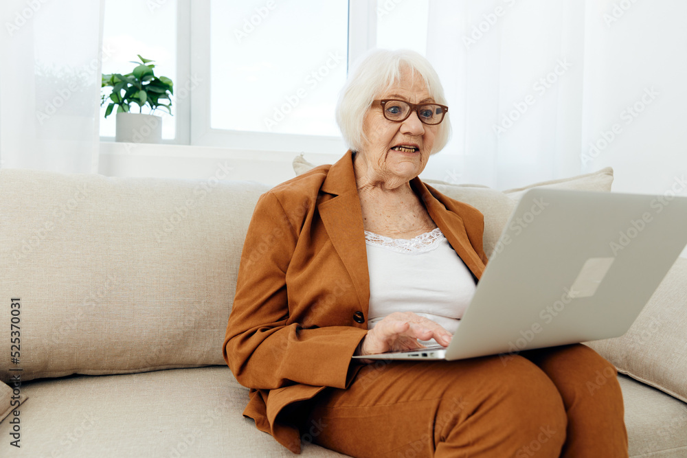 an experienced, adult woman is sitting on the couch working remotely at a laptop, working intently in a comfortable environment an experienced, adult woman is sitting on the couch working remotely at a laptop, working intently in a comfortable environment