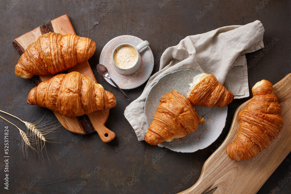 Kitchen boards, plate with tasty croissants and cup of coffee on dark table, closeup. French pastry. Top view