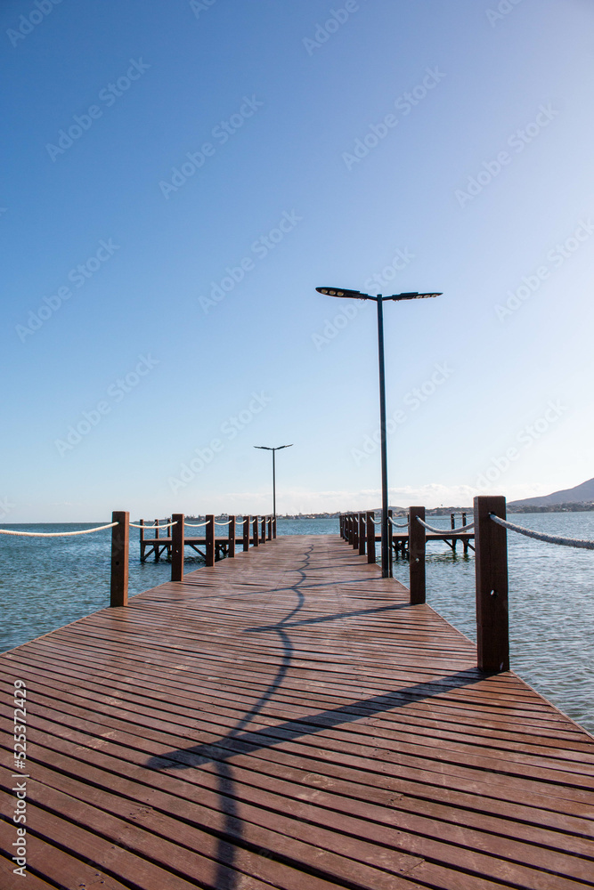 Wooden pier with lampposts at Sao Pedro da Aldeia beach on a sunny day, Cabo Frio, Brazil.