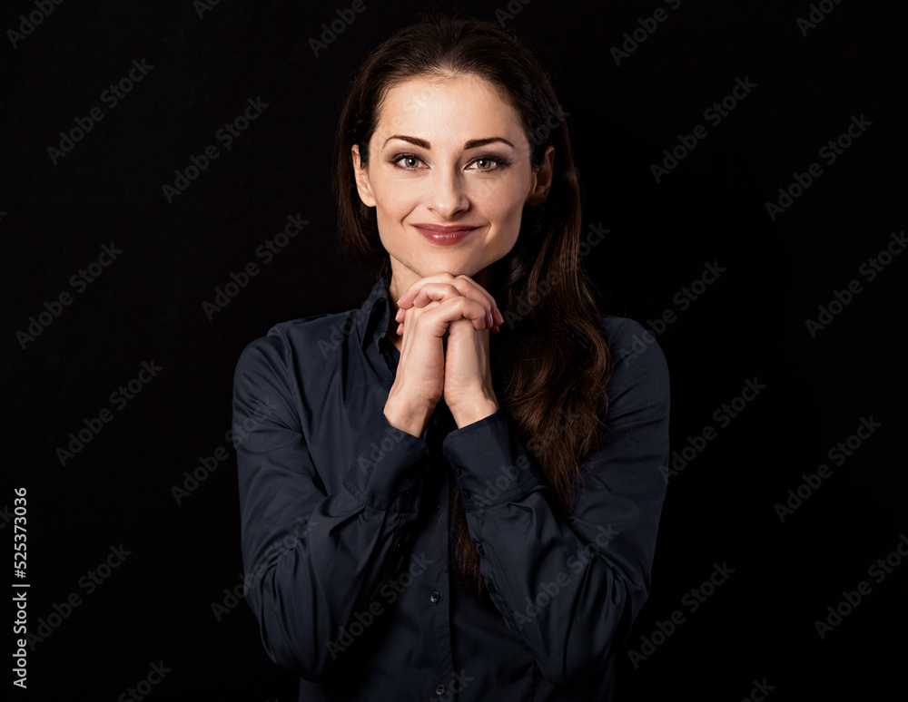 Beautiful thinking smiling business woman with hands under the face in blue shirt on black background with empty copy space for text. Closeup Beautiful thinking smiling business woman with hands under the face in blue shirt on black background with empty copy space for text. Closeup