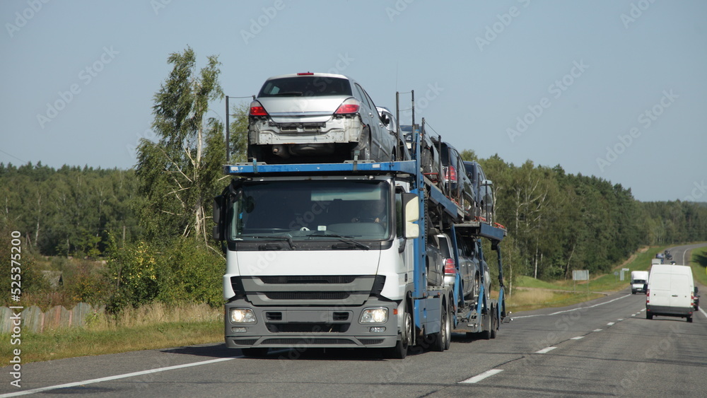 Loaded car carrier truck with old cars transporter semi trailer drive on suburban highway road at summer day, front side view. European used cars export in Russia with sanctions