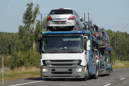 Loaded two level car carrier truck with car transporter semi trailer drive on suburban highway road at summer day, front side view. Delivery autos logistics, automobile transportation © Ilya