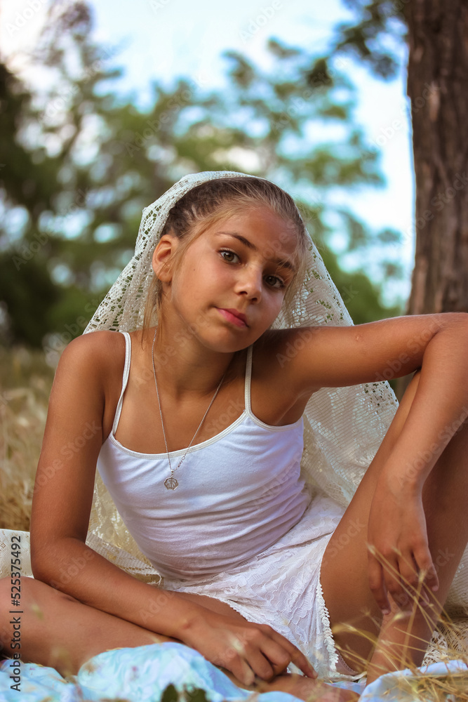 Portrait of a beautiful mixed race teenage girl in white clothing sitting outdoors at a picnic in summer day. Schoolgirl on vacation on nature Self-confident girl posing for a camera. Book cover photo Portrait of a beautiful mixed race teenage girl in white clothing sitting outdoors at a picnic in summer day. Schoolgirl on vacation on nature Self-confident girl posing for a camera. Book cover photo