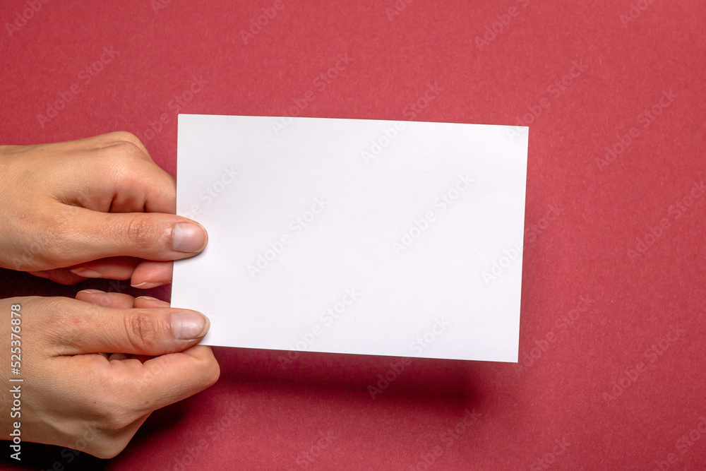Obraz premium two female hands holding a blank piece of paper with copy space in front of a red background cardboard