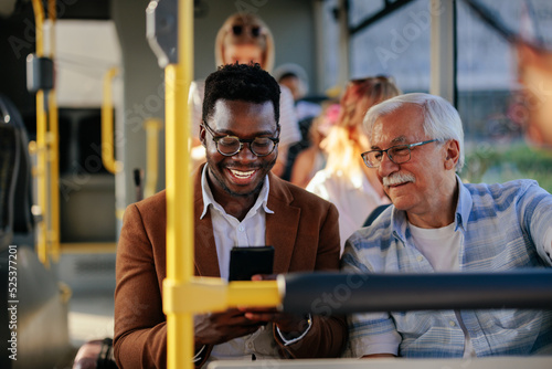 Fototapeta Black man showing senior caucasian man smartphone on public transport