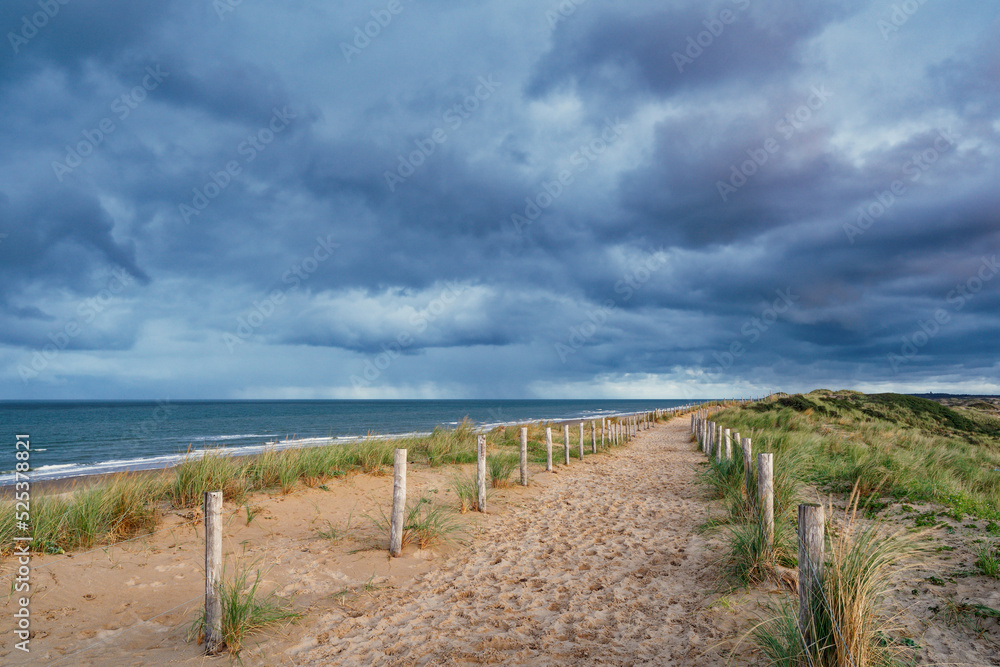 A beautiful sandy path along the ocean. Dark clouds in the sky. North Holland dune reserve, Egmond aan Zee, Netherlands.