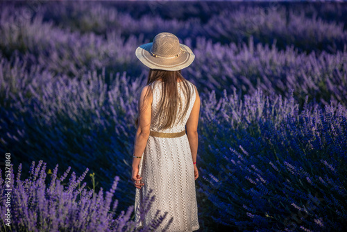 Charming Young woman with a hat and white dress in a purple lavender field at sunset. LIfestyle outdoors. Back view stock photo