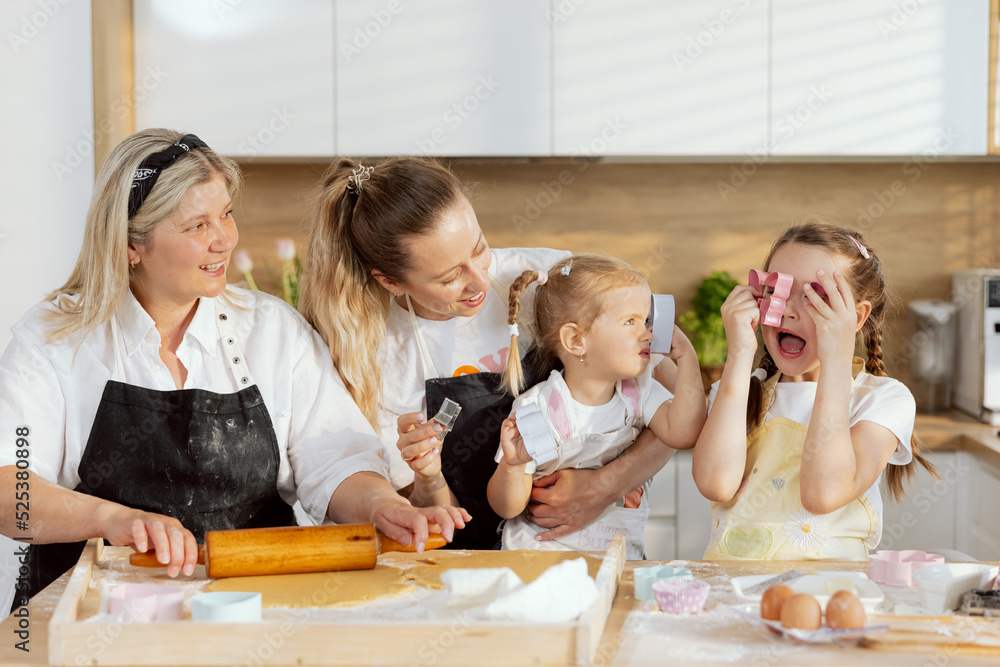 Beautiful family in modern kitchen wearing aprons baking cooking. Edlery grandmother teaching rolling dough young mother holding preschooler daughter watching process. Beautiful family in modern kitchen wearing aprons baking cooking. Edlery grandmother teaching rolling dough young mother holding preschooler daughter watching process.
