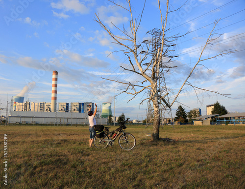Mężczyzna z rowerem turystycznym przed uschniętym drzewem brzozy, elektrownia.