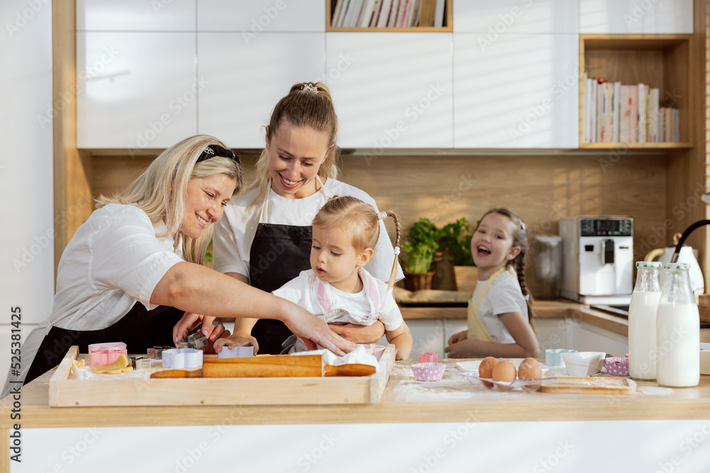 Delighted preschooler daughter pressing cookies with cookies cutter. Young delighted mother and granny smiling watching process teaching offsprings baking cooking homemade cookies for Christmas. Delighted preschooler daughter pressing cookies with cookies cutter. Young delighted mother and granny smiling watching process teaching offsprings baking cooking homemade cookies for Christmas.