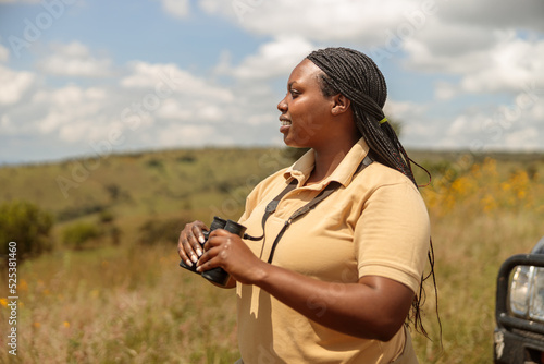 Side view of emale tour guide using binoculars and searching the landscape for wildlife in Africa