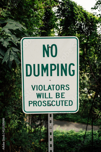 green and white metal "No Dumping" warning sign, violators will be prosecuted