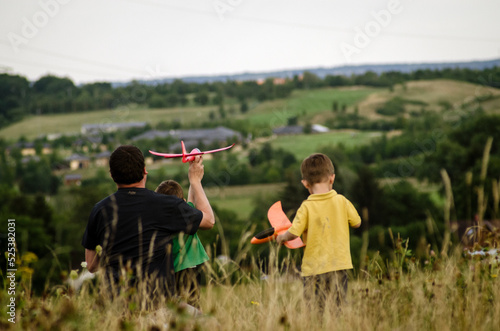 dad with two children are throwing airplanes in nature on a hill with a beautiful view