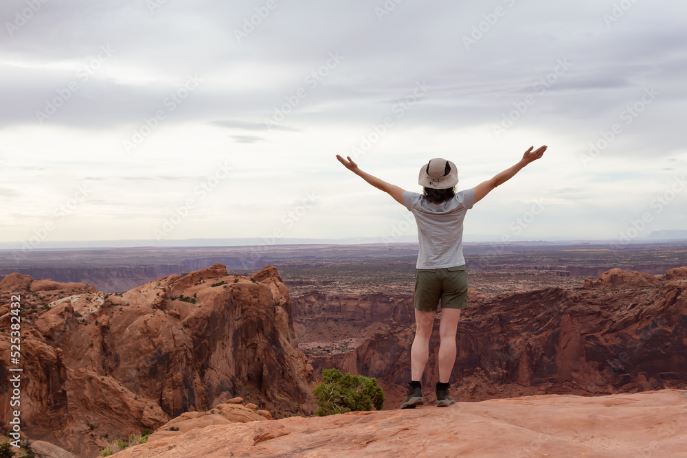 Adventurous Woman Hiking at a Desert Canyon with Red Rock Mountains. Cloudy Sky. Canyonlands National Park. Utah, United States. Adventure Travel Adventurous Woman Hiking at a Desert Canyon with Red Rock Mountains. Cloudy Sky. Canyonlands National Park. Utah, United States. Adventure Travel