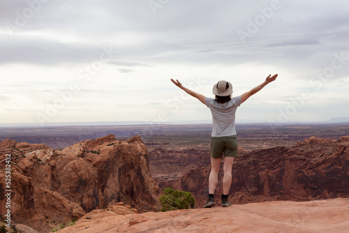 Adventurous Woman Hiking at a Desert Canyon with Red Rock Mountains. Cloudy Sky. Canyonlands National Park. Utah, United States. Adventure Travel