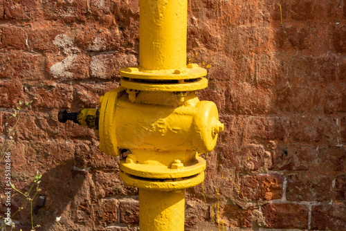 Yellow gas pipe with a tap on the background of a brick house. Old gas valve in yellow paint.