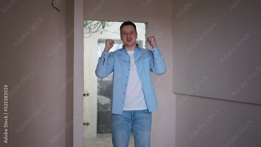 Portrait of excited Caucasian young man entering new flat gesturing yes smiling looking at camera. Happy successful apartment owner posing in building under construction indoors Portrait of excited Caucasian young man entering new flat gesturing yes smiling looking at camera. Happy successful apartment owner posing in building under construction indoors