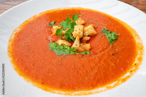 A traditional dish of Spanish and Italian cuisine is tomato soup with croutons and pesto sauce on a plate.