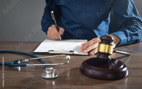 Man signing in document. Judge gavel and stethoscope on the table