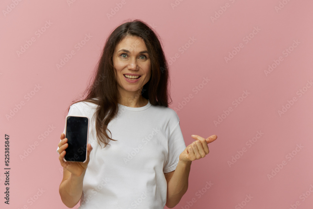 a beautiful, happy woman in a light t-shirt holds out her phone to the camera showing the screen. Horizontal photo on a plain background with empty space for an advertising insert a beautiful, happy woman in a light t-shirt holds out her phone to the camera showing the screen. Horizontal photo on a plain background with empty space for an advertising insert