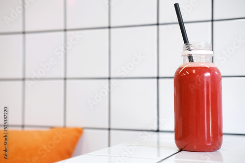 Freshly squeezed watermelon juice in a plastic bottle with straws on a background of white ceramic tiles.