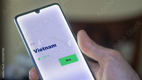 An investor's analyzing the Vietnam etf fund on screen. A phone shows the Vietnamese market ETF's prices to invest