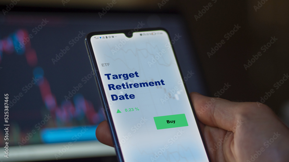 An investor's analyzing the target retirement date etf fund on screen. A phone shows the ETF's prices target retirement date to invest An investor's analyzing the target retirement date etf fund on screen. A phone shows the ETF's prices target retirement date to invest