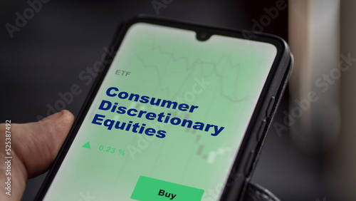 An investor's analyzing the consumer discretionary equities etf fund on screen. A phone shows the ETF's prices consumer discretionary equity to invest