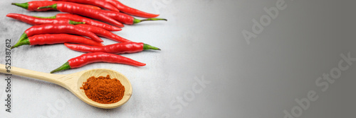 Ground red hot peppers in a wooden spoon and hot chili pods in the background. Spice for cooking spicy dishes. Banner with free space for text