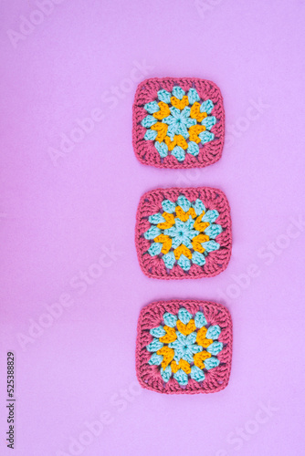 Vertical row of three crochet granny square pieces on light violet background.