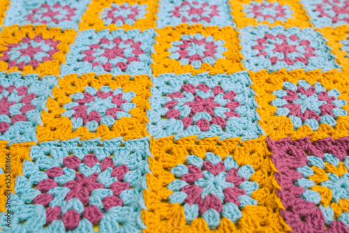 Side view of multicolored crochet granny squares, seamed together in a blanket. © Uliana