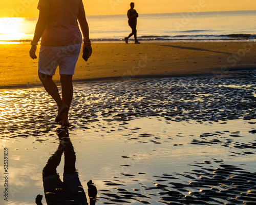Two people walking on beach at sunrise,reflections on tidal flats,Hilton Head Island SC.