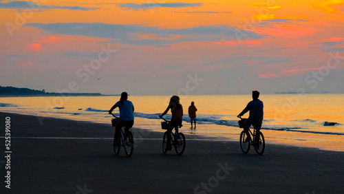 Sunrise at beach with silhouetted family on bicycles.
