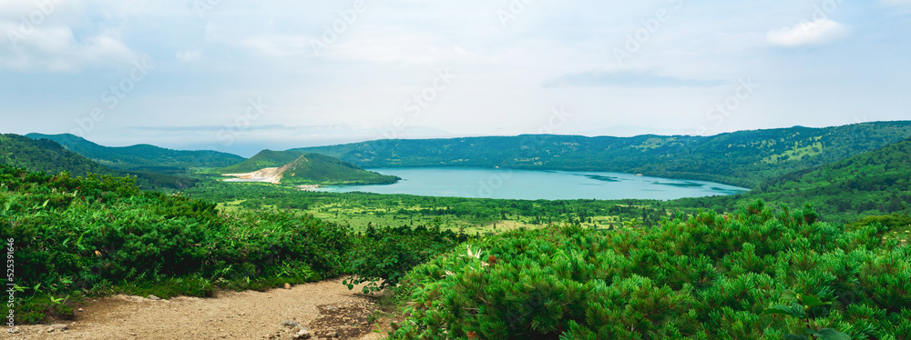 natural landscape of Kunashir island, view of the Golovnin volcano caldera with hot lakes and a path through the thickets of sasa and dwarf pines on a foreground