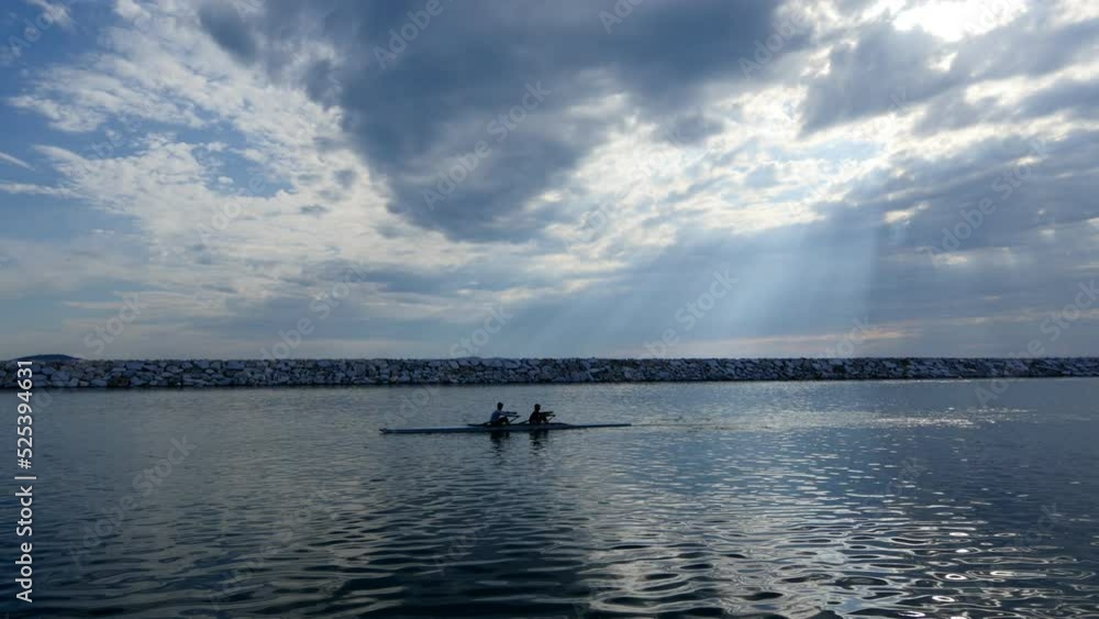 Young single scull rowing competitors paddle on the tranquil lake. Beautiful beams of the sunshine filter through clouds
Young single scull rowing competitors paddle on the tranquil lake. Beautiful beams of the sunshine filter through clouds