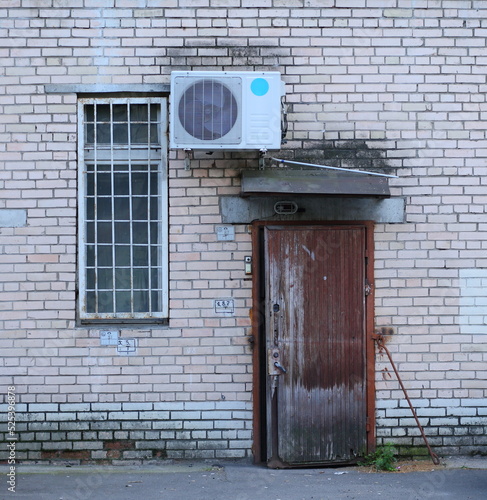 Wooden door and barred window in a white brick wall with air conditioning, Bolshevikov Avenue, St. Petersburg, Russia, August 2022 photo