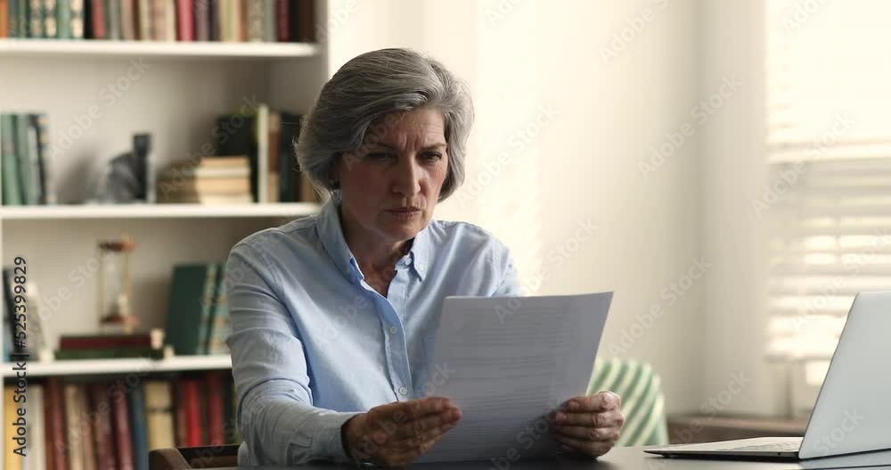 Hoary elderly senior woman reading paper document at work table, turning from serious to frustrated, shocked, desperate, getting bad news, bank, eviction notice, medical test result