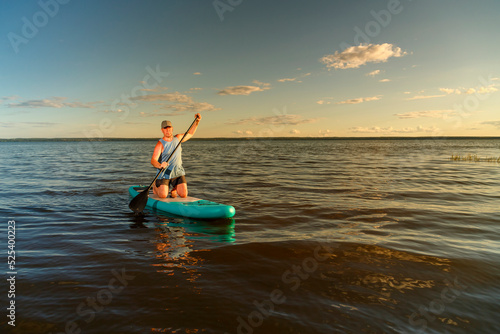 a man in shorts stands with a paddle on a SUP board at sunset in the lake.