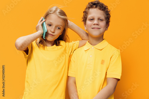cute, funny children, school age, brother and sister stand on a yellow background and talk on the phone