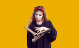 Woman dressed in Halloween costume reading book of spells, choosing death hex and learning about magic. Young witch or devil looking through witchcraft manual or studying guide book for evil monsters