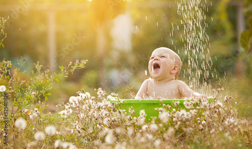 A small child plays in a bowl of water in a summer garden on a sunny day © oes