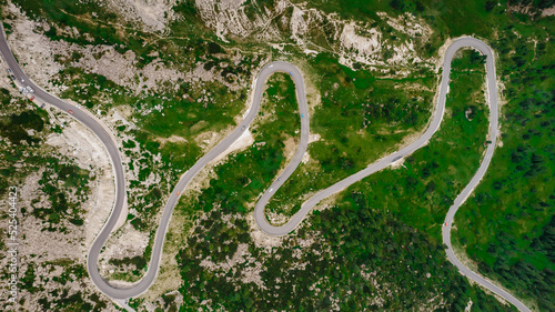Winding road from high mountain pass in Dolomites, Italy. Great road trip through dense woods and meadows. Aerial view. Curvy road in summer forest scenery, mountain landscape.Top Down Birds Eye View.