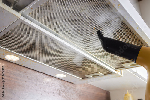 house cleaning. Girl brushes steam cleaners kitchen drawing with steam in green gloves. cleaning of a surface. photo