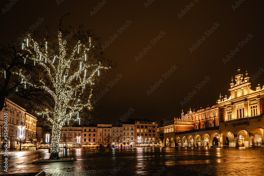 Krakow after rain,Poland.Main square with famous Christmas markets,Rynek Glowny at night with reflection,decorated Xmas tree.Festive atmosphere,blurred people in motion,illuminated night city