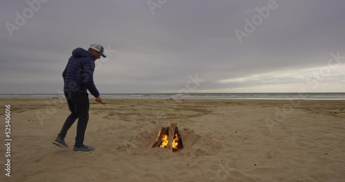 Man squats near fireplace on beach at Oceano Dunes SVRA at Pismo Beach, California photo