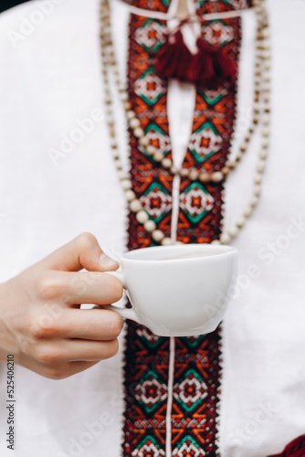 A guy in an embroidered shirt holds a cup of coffee in his hands.Coffee love concept.