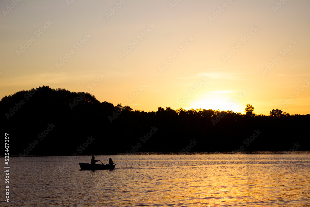 A young man and a girl are sitting in a boat and floating on the river at sunset. Silhouette of a couple